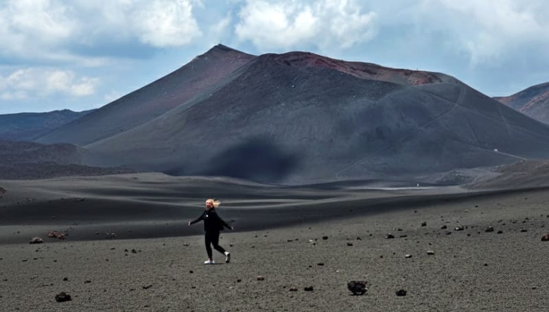 Hiker crossing the black volcanic desert below the craters of Mount Etna