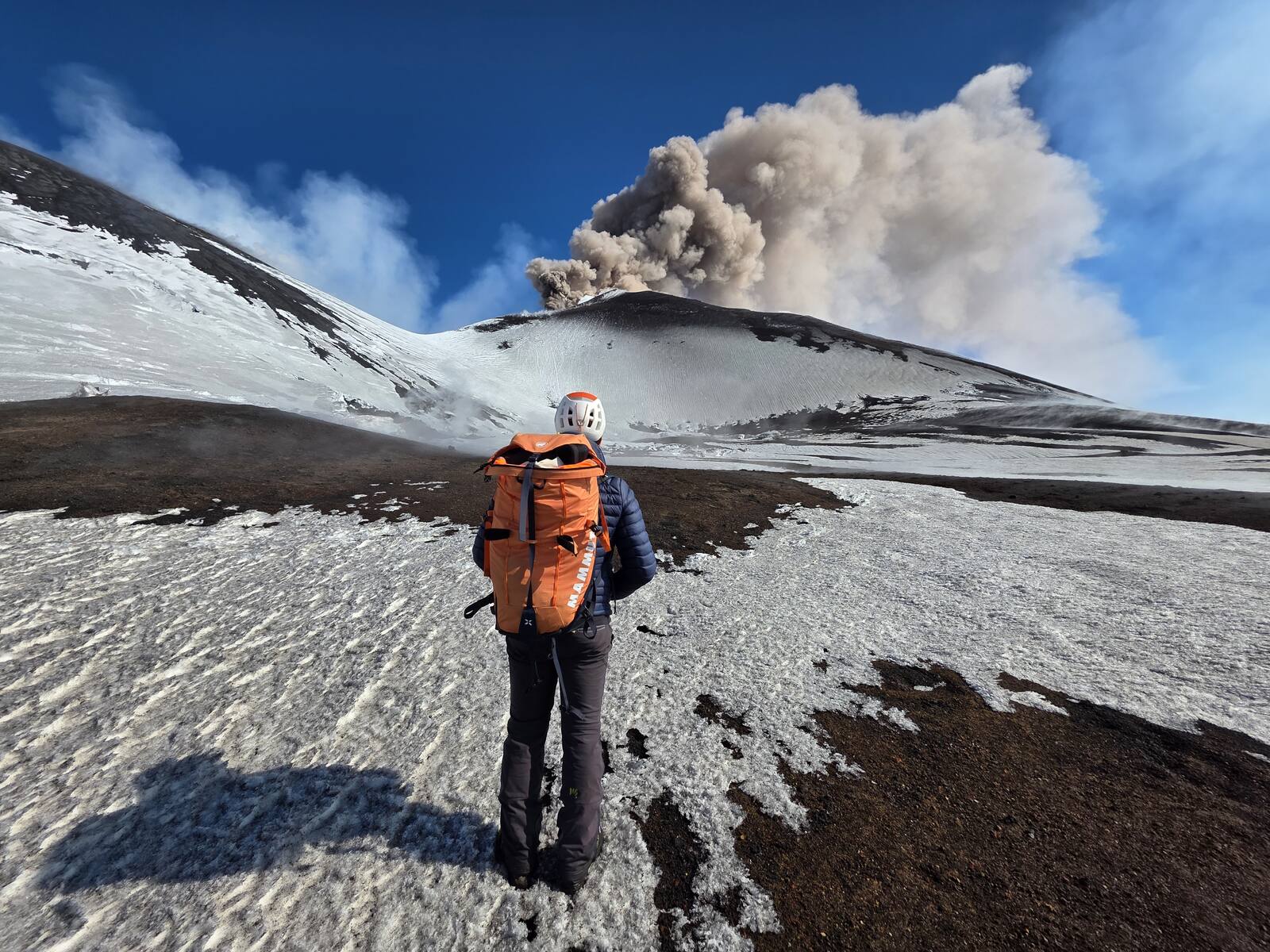 A guide walking towards Etna's smoking summit crater across the snow