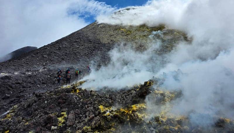 Excursionistas ascendiendo entre fumarolas por el sendero sumital del Etna
