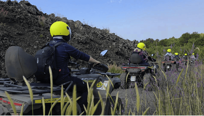 Close-up of quad riders wearing yellow helmets crossing volcanic terrain on Mount Etna
